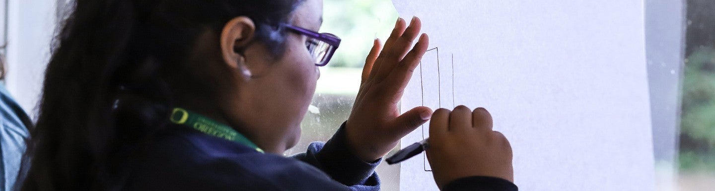 sail student draws shapes on white paper held up to window