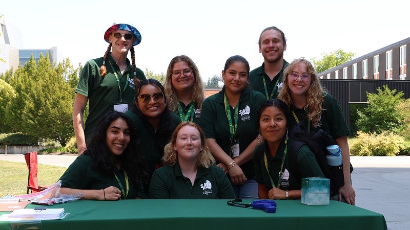 SAIL participants stand and sit at table with logo on tablecloth