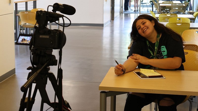 SAIL student sits at desk facing camera equipment