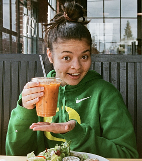FIG Assistant Eve Posner holding a smoothie above a plate of food, looking excited.