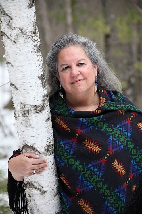 Photo of author Robin Wall Kimmerer leaning against a tree trunk